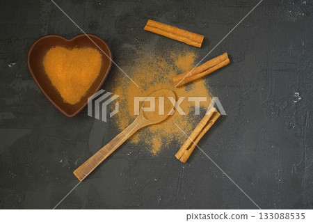 Cinnamon powder in heart shaped bowl on black stone table. Love concept. Top view flat lay with copy space Cinnamon powder in heart shaped bowl on black stone table. Love concept. Top view flat lay with copy space 133088535