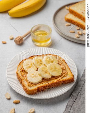 Peanut butter toast and banana in a white plate on a light background with honey Peanut butter toast and banana in a white plate on a light background with honey 133088836