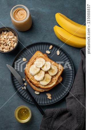 Peanut butter toast and banana on a black plate on a dark background with nuts 133088837