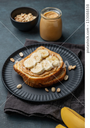Peanut butter toast and banana on a black plate on a dark background with nuts 133088838