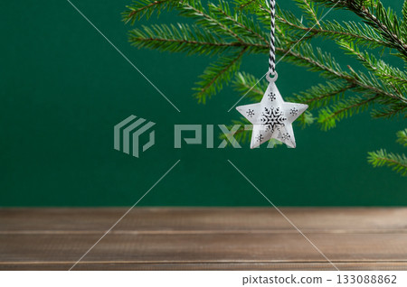 Fir branches with a star-shaped Christmas tree ornament on a green and dark wooden background. 133088862
