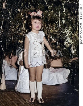Vintage portrait of a girl dressed as a snowflake singing a song near a Christmas tree. Retro photo 1973. Vintage portrait of a girl dressed as a snowflake singing a song near a Christmas tree. Retro photo 1973. 133089015