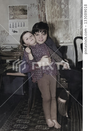 A vintage portrait of a sister and brother near a New Year's tree. A girl with bows hugs her brother. Retro 1973 133089018