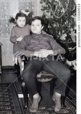 A vintage portrait of a sister and brother near a New Year's tree. A girl with bows hugs her brother. Retro 1973 133089019