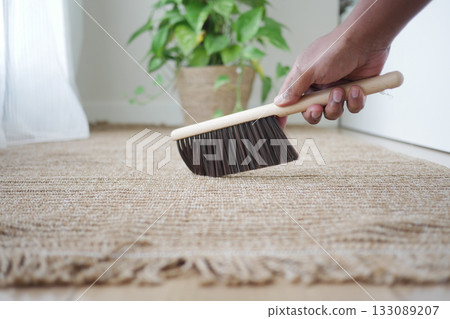 Cleaning a rug with a broom in a bright room Cleaning a rug with a broom in a bright room 133089207