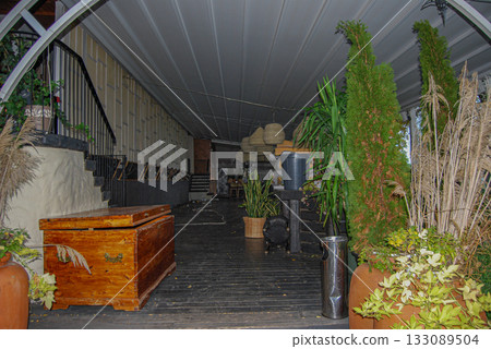 Long covered hallway with rustic decor and lush greenery. Indoor corridor with rustic decor features wooden floors and a wooden chest. 133089504