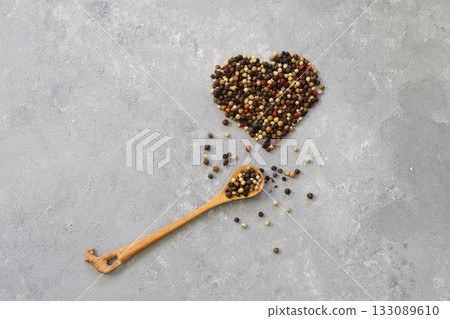 Mixture of peppercorns in heart shape isolated on white background. With wooden spoon. Mixture of peppercorns in heart shape isolated on white background. With wooden spoon. 133089610