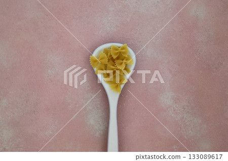 Raw pasta farfalle on wooden spoon on black background. Top view of Italian cuisine ingredient. 133089617