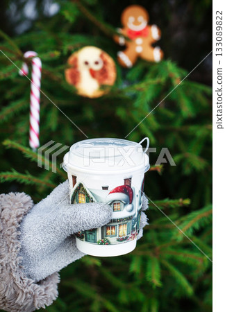 Woman`s hand hold a cup of coffee on Christmas cookies and fir-tree background, outdoor 133089822