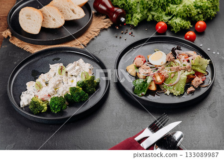 Two plated dishes: creamy chicken with broccoli and tuna salad with egg on dark table Two plated dishes: creamy chicken with broccoli and tuna salad with egg on dark table 133089987