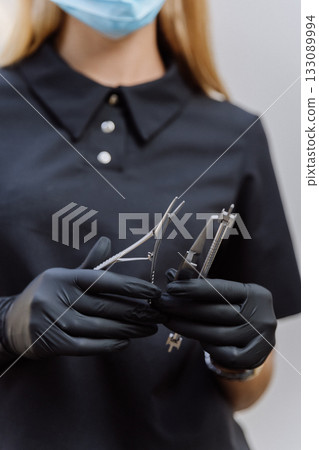 Dentist in mask and black gloves holding sterile dental instruments, clinic closeup 133089994