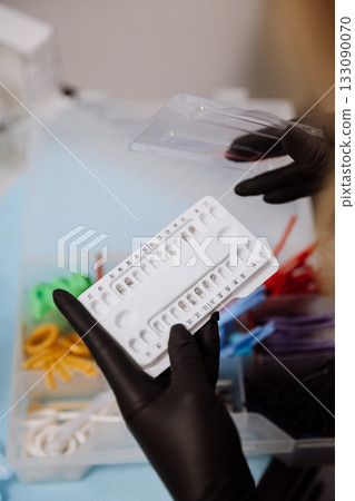 Orthodontic brackets in numbered tray held by gloved clinician, dental clinic closeup Orthodontic brackets in numbered tray held by gloved clinician, dental clinic closeup 133090070