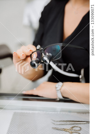 Clinician holding dental loupes for precision work, with tools on table, clinic closeup 133090071