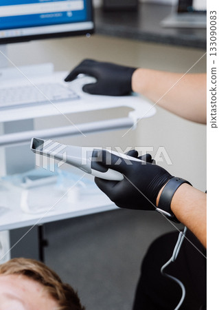 Dentist holding intraoral scanner near computer during digital dental exam 133090083