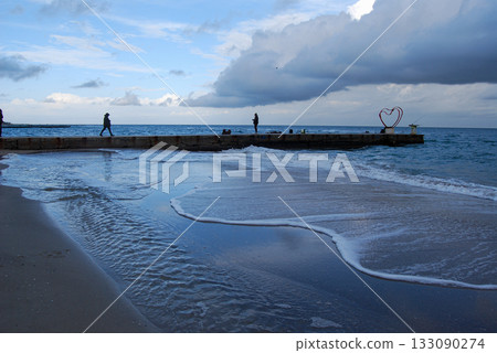 Coastal serenity waves kissing the shoreline under a cloudy sky. The image captures a serene coastal scene with waves gently lapping against the sandy shoreline under a cloudy sky. 133090274