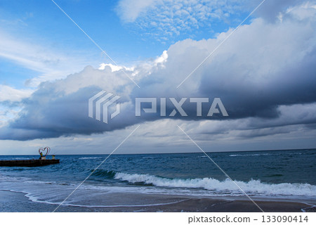 Coastal serenity waves kissing the shoreline under a cloudy sky. The image captures a serene coastal scene with waves gently lapping against the sandy shoreline under a cloudy sky. 133090414