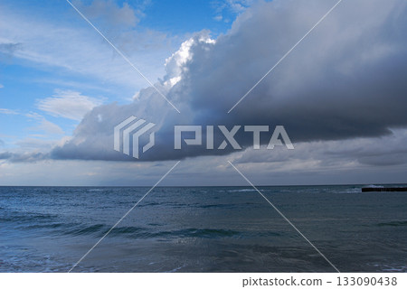 Dramatic ocean view with approaching storm clouds. Expansive sea view under a sky filled with thick, dark storm clouds approaching from the right.  133090438