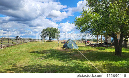 Camping in a tranquil setting with clouds and open fields under a blue sky during the day 133090446