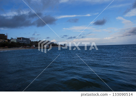 View of the coastal slopes of Odessa with a dark bay and cloudy sky. Dark, cloudy sky looms over a seaside town along the coast. The sea is deep and choppy, stretching towards the horizon.  133090514