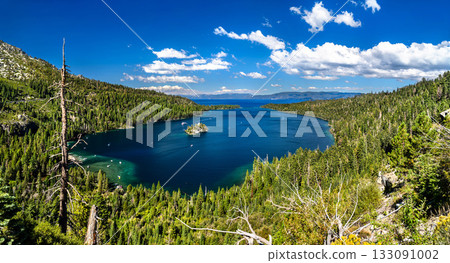 Panoramic view of Emerald Bay and Fannette Island in Lake Tahoe. The deep blue water is surrounded by pine forests under a cloudy sky 133091002