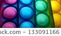 Vibrant rainbow pop it fidget toy close-up. Close-up of a multicolored pop it fidget toy, featuring rows of bubble-like protrusions in vibrant colors: red, orange, yellow, green, blue, and purple. 133091166