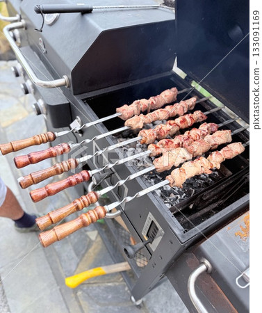Juicy grilled meat skewers cooking on hot charcoal barbecue, traditional shashlik on metal skewers with smoke and flame Juicy grilled meat skewers cooking on hot charcoal barbecue, traditional shashlik on metal skewers with smoke and flame 133091169