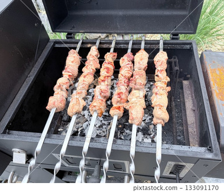 Juicy grilled meat skewers cooking on hot charcoal barbecue, traditional shashlik on metal skewers with smoke and flame, outdoor picnic or BBQ party scene, close-up of delicious roasted meat 133091170