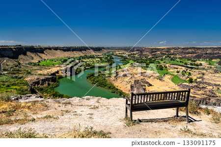 Empty bench overlooking the scenic Snake River Canyon in Twin Falls, Idaho. The green river and a golf course are visible below under a clear blue sky Empty bench overlooking the scenic Snake River Canyon in Twin Falls, Idaho. The green river and a golf course are visible below under a clear blue sky 133091175