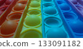 Vibrant rainbow pop it fidget toy close-up. Close-up of a multicolored pop it fidget toy, featuring rows of bubble-like protrusions in vibrant colors: red, orange, yellow, green, blue, and purple. 133091182