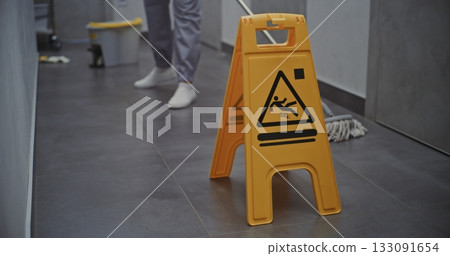 Maid Carefully Washes Floor While Bright Yellow Warning Sign Stands Beside 133091654