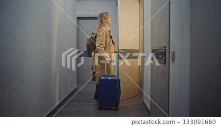 Woman With Suitcase Walks Through Quiet Hotel Corridor, Searching For Room Woman With Suitcase Walks Through Quiet Hotel Corridor, Searching For Room 133091660