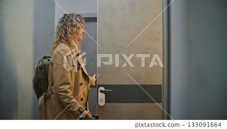 Female Guest With Backpack And Rolling Suitcase Moves Through Minimalist Hotel Corridor Female Guest With Backpack And Rolling Suitcase Moves Through Minimalist Hotel Corridor 133091664