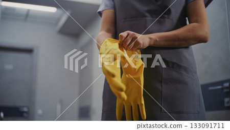 Careful Preparation on Cleaning. Hotel Housekeeper in Uniform Puts on Bright Yellow Cleaning Gloves 133091711
