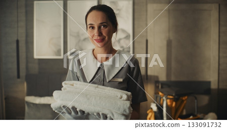 Friendly Female Hotel Housekeeper Carrying Neatly Folded Towels in Modern Hotel Suite 133091732