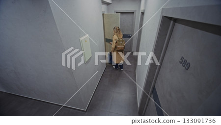 Stylish Female Traveler in Light Trench Coat Walks Down Hotel Corridor 133091736