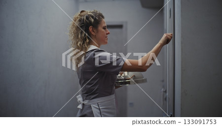 Friendly Female Hotel Attendant in Grey Uniform Delivering Room Service 133091753