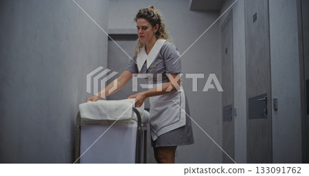 Hotel Cleaning Staff Woman Stands By Housekeeping Cart, Folding Towels With Smooth 133091762