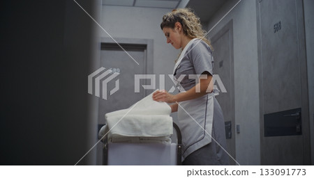 Hotel Cleaning Staff Woman Stands By Housekeeping Cart, Folding Towels With Smooth 133091773