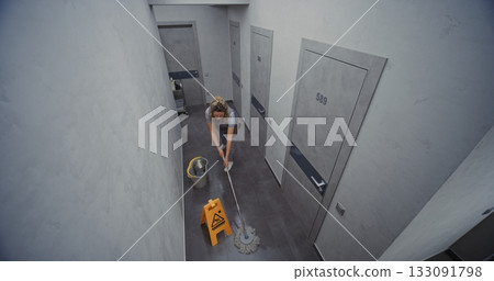 Hotel Cleaning Attendant in Professional Uniform Carefully Mops Hotel Hallway Floor 133091798