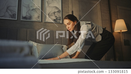 Housekeeping Woman Employee in Uniform Adjusts Bedding and Pillow Placement 133091815