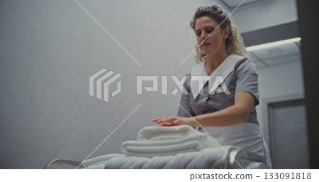 Smiling Maid in Professional Uniform Arranges Crisp, Freshly Laundered Towels on Housekeeping Cart Smiling Maid in Professional Uniform Arranges Crisp, Freshly Laundered Towels on Housekeeping Cart 133091818