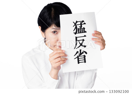 A senior woman holds a piece of paper with the words "deep remorse" written on it and looks at it timidly A senior woman holds a piece of paper with the words "deep remorse" written on it and looks at it timidly 133092100