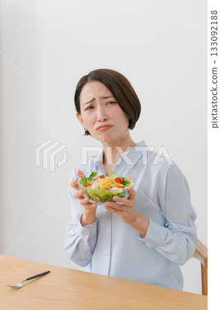 A woman with a troubled expression holding a salad 133092188