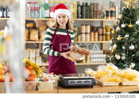 Female vendor in a Santa Claus hat offers to buy nougat for festive table on Christmas Female vendor in a Santa Claus hat offers to buy nougat for festive table on Christmas 133093185