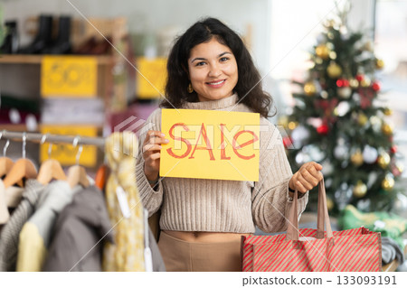 Latina woman standing in a store at a Christmas sale with a yellow poster Latina woman standing in a store at a Christmas sale with a yellow poster 133093191