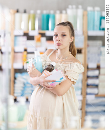 Happy young pregnant woman with full arms choosing something in drugstore 133093562