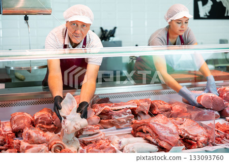 Near counter mature male seller offers shows pork ear in butcher shop 133093760