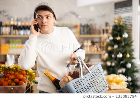 Guy wander around store, puts purchases in basket and chats speak on phone with friend, New Year Eve 133093784