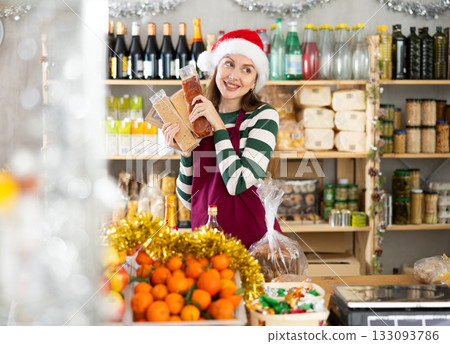 Female vendor in a Santa Claus hat offers to buy nougat for festive table on Christmas Female vendor in a Santa Claus hat offers to buy nougat for festive table on Christmas 133093786