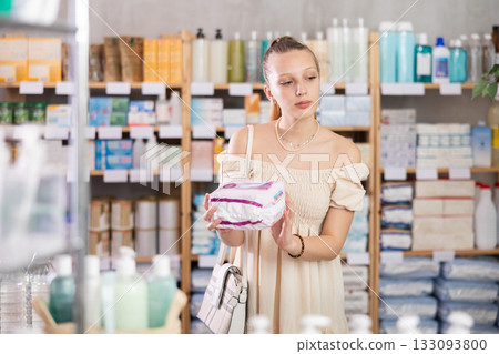 Young woman chooses feminine pads at pharmacy 133093800